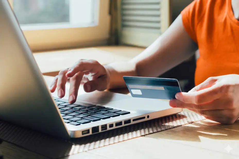 A person typing on a laptop while holding a credit card.